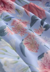 Gėlių audinys su rožiniais ir baltais žiedais šviesiai mėlyname fone, tekstūruota paviršiaus struktūra ir minkštas kritimas.