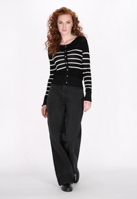 Cardigan a righe bianche e nere con scollatura rotonda e chiusura con bottoni, abbinato a pantaloni neri larghi e calzature nere. Texture liscia.