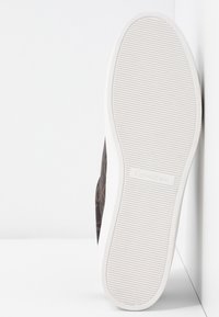 Sneakers Calvin Klein z ciemnym wzorzystym wierzchem, białą gumową podeszwą z teksturowanymi paskami oraz logo na pięcie.