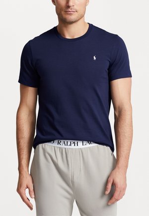 Marineblauw katoenen t-shirt met een ronde hals, korte mouwen en een klein wit logo op de linkerborst. Gepaard met grijze broek met elastische taille.