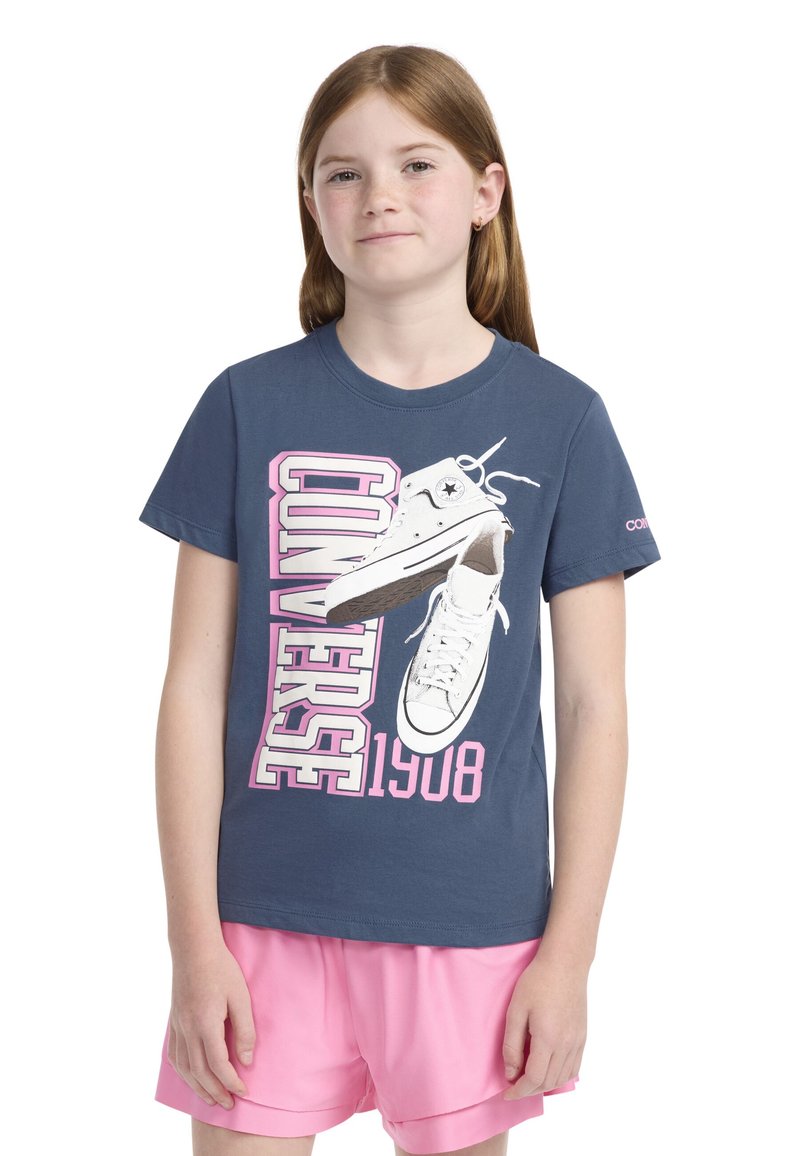 Námořnická modrá bavlněná tričko s grafikou bílých vysokých tenisek a tučným růžovým textem "CONVERSE 1908." Krátké rukávy, kulatý výstřih.