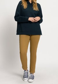 Marinblå sweatshirt med avslappnad passform, i kombination med slim-fit byxor i senapsgul och blå sneakers med vita snörningar och minimala detaljer.