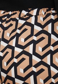 Grafisch patroon broek, met zwart, wit en beige geometrische ontwerpen. Elastische tailleband met gerimpelde rand. Zachte, gladde stofstructuur.