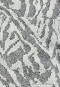 Szary i biały sweter z teksturowanym, abstrakcyjnym wzorem. Miły w dotyku materiał z widoczną metką logo i szytymi szwami.