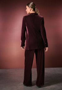 Burgundy velvet pantsuit with a tailored blazer and wide-leg trousers; features smooth texture and fitted design with button accents.