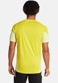 T-shirt de sport jaune à manches courtes, fabriqué dans un matériau léger, à la texture lisse, avec un design de panneaux latéraux contrastants.