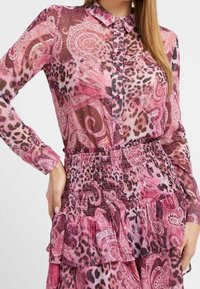 Camicia a maniche lunghe rosa con motivi paisley e stampa leopardata. Presenta una chiusura con bottoni sul davanti, un colletto e una vita arricciata con orlo arruffato.