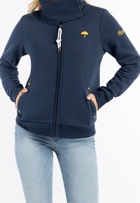 Felpa navy con zip e colletto alto, cordino bianco e logo dell'ombrello giallo. Presenta due tasche frontali con accenti di bottone giallo.
