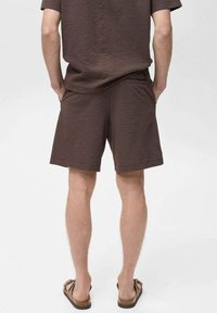 Shorts marron texturés et haut à manches courtes assorti, vus de dos. Tissu léger, coupe décontractée, complétés par des tongs marron.