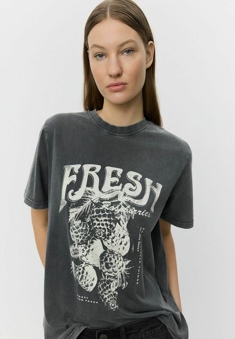 Pilkas per didelis t-shirt, pagamintas iš medvilnės, su baltu ananasų grafikiniu spaudiniu ir žodžiu "FRESH" ryškiu šriftu.