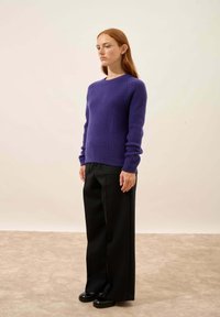 Violetti neulepaita, jossa on ribbipinta, pyöreä pääntie ja pitkät hihat, yhdistettynä leveisiin mustiin housuihin ja mustiin kenkiin.
