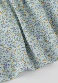 Jasnoniebieska tkanina z drobnym pomarańczowo-fioletowym wzorem kwiatowym, delikatnie marszczona z widocznymi fałdami i zagnieceniami.