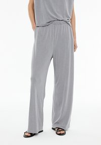 Helle graue weite Hosen aus weichem Stoff, die einen lässigen Schnitt, einen elastischen Bund und eine dezente gerippte Textur aufweisen. Kombiniert mit schwarzen Sandalen.