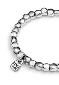 Pulsera de cuentas plateadas con eslabones de formas irregulares y un pequeño dije rectangular grabado con "UNO de 50."