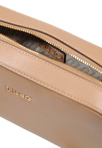 Bolsa de cuero beige con superficie texturizada, cremallera dorada e interior estampado. Logo visible en el exterior.