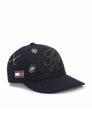 Marineblaue Baseballkappe mit besticktem "TH" und vier Metall-Pins: gekreuzte Golfschläger, Löwenkopf, Schild und rot-weiß-blaues Flaggenmotiv.