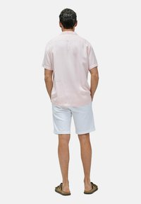 Lichtroze shirt met korte mouwen, witte shorts en bruine sandalen. Zachte stof, casual pasvorm, knoopsluiting aan de achterkant en omgeslagen mouwen.
