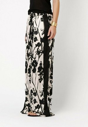 Woman wearing black and white floral wide-leg pants with black side stripes, paired with black top and gold cuff bracelet.