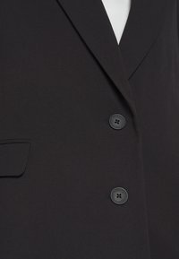 Blazer noir avec une texture de tissu lisse, des revers crantés, deux boutons et une poche poitrine.