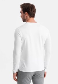Witte, lange mouwen shirt gemaakt van zachte katoen, met een ronde hals en een aansluitend ontwerp, gezien vanaf de achterkant met een neutrale achtergrond.