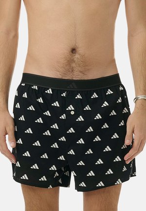 Schwarze Badeshorts mit einem weißen Dreiecksmuster, elastischem Bund und einem einzelnen Knopfverschluss. Hergestellt aus leichtem Stoff.
