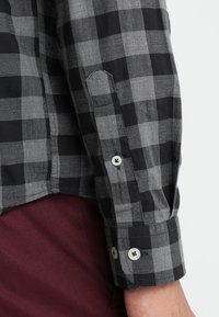 Zwarte en grijze geruite blouse met lange mouwen en verstelbare manchetten, voorzien van een knoopdetail en een gestructureerde stof.