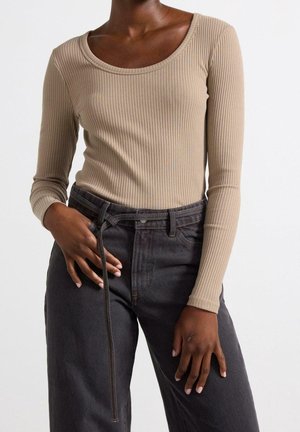 Person wearing a beige ribbed long-sleeve top tucked into high-waisted dark grey jeans with a tied belt.