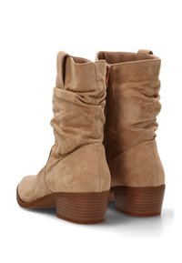 Un par de botas de ante color beige hasta la mitad de la pantorrilla, con tacones bajos apilados y cremalleras laterales, que presentan un diseño arrugado en el eje.