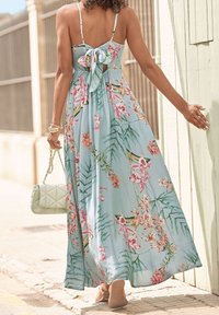 Maximekkokki vaaleansinisestä kankaasta, jossa on kukka- ja lehtikuvioita, selkäsolmimismalli, spagettiolkaimet, yhdistettynä tikkikuvioiseen vaaleanvihreään käsilaukkuun.