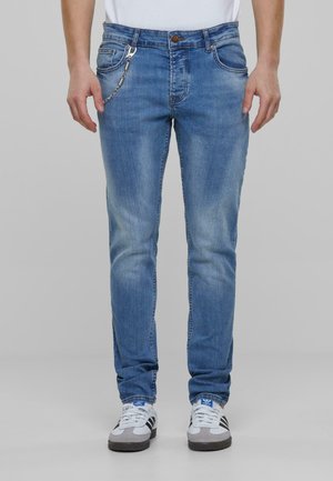 Blå denimjeans med slim fit, som har en lommekjede, lys fading og standard femlomme-design. Brukt med grå og hvite sneakers.