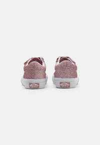 Ružové trblietavé nízke tenisky s bielymi gumovými podrážkami, polstrovaným golierom a červeným logom Vans na päte. Elastické šnúrky pre jednoduché obúvanie.