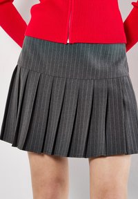 Gonna plissettata grigia a righe con vita aderente, realizzata in tessuto testurizzato, abbinata a un maglione rosso a coste.