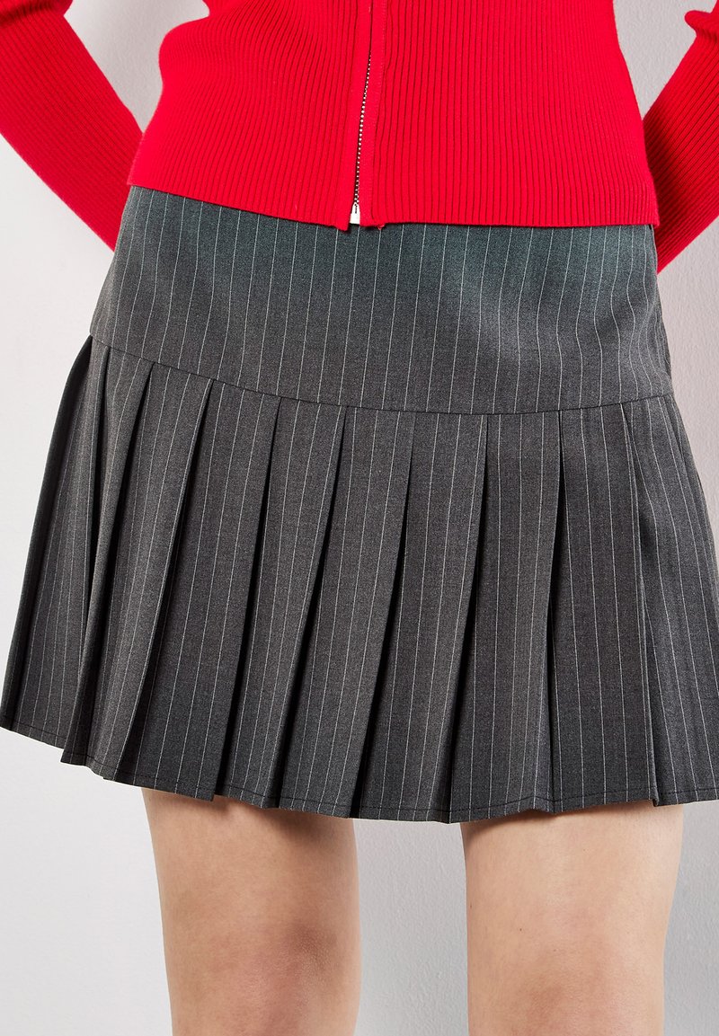 Gonna plissettata grigia a righe con vita aderente, realizzata in tessuto testurizzato, abbinata a un maglione rosso a coste.