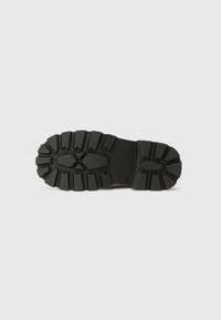 Semelle de chaussure en caoutchouc noir avec un motif de semelle robuste, présentant des rainures profondes et une surface texturée pour une meilleure adhérence et durabilité.