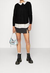 Svart långärmad tröja med vit krage, lager på lager över en vit skjorta, parat med en grå minikjol och svarta snörkängor. Iriserande handväska.