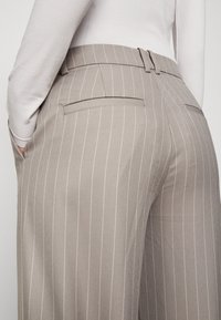 Lichtgrijze broek met streepjes in een getailleerde pasvorm, met een platte voorkant, twee achterzakken en een gladde textuur.