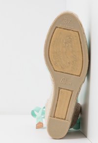 Semelle d'espadrille tissée en beige clair avec des accents de ruban vert menthe. Présente la taille 37 et l'impression "Fabriqué en Espagne" au fond.