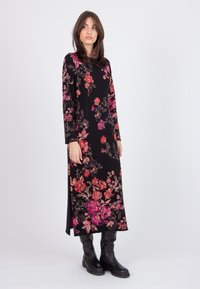 Long black dress with bright floral pattern in pink and red, round neckline, long sleeves, side slits, worn with black knee-high boots.