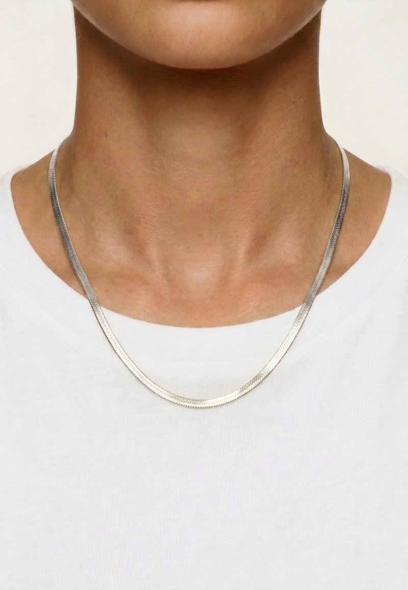 Gros plan sur un cou portant un collier chaîne argenté lisse sur une chemise blanche.