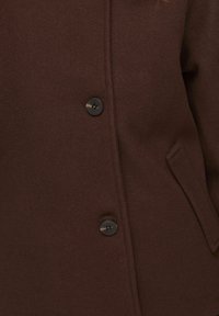 Manteau en laine marron avec deux boutons foncés et une poche inclinée sur le côté droit, montrant les détails de la partie centrale avant.