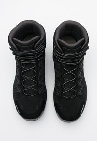 Zapatillas deportivas negras de corte medio con parte superior de malla texturizada, acentos reflectantes y un sistema de cordones intrincado. Cuenta con un collar y una suela acolchados.