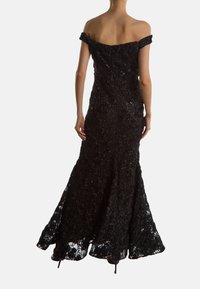 Svart spetsklänning för kvällsbruk med axelbandslösa ärmar, figursydd ovandel och utsvängd kjol. Har intrikata blommönster och en strukturerad finish.