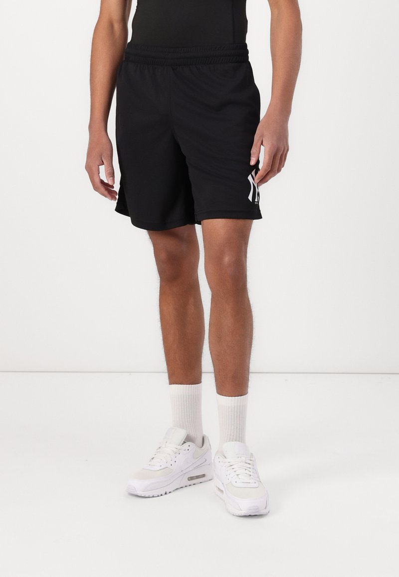 Shorts deportivos negros con cintura elástica y acentos de logo blanco en el costado. Se llevan con zapatillas blancas y calcetines de longitud barco.