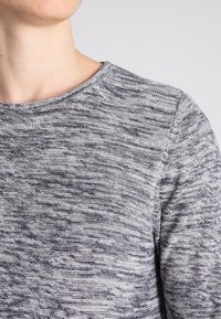 Maglione grigio a maglia testurizzata con scollo rotondo e un motivo sottile. Presenta cuciture visibili lungo il colletto e le cuciture delle spalle.