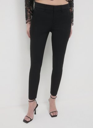 Pantalon noir ajusté à coupe slim, avec une taille plate, des passants de ceinture et une texture lisse. Porté avec des talons noirs à brides.