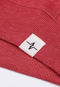 Rood ribbelstof gedeelte met een gestructureerde afwerking, voorzien van een wit label met zwarte grafische accenten, genaaid in de zoom.