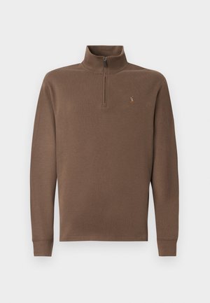 Brun pullover med høj krave og lynlås, lavet af blødt materiale. Har lange ærmer og et lille logo på brystet.
