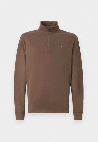 Bruine pullover met een hoge kraag en ritssluiting, gemaakt van zacht materiaal. Heeft lange mouwen en een klein logo op de borst.