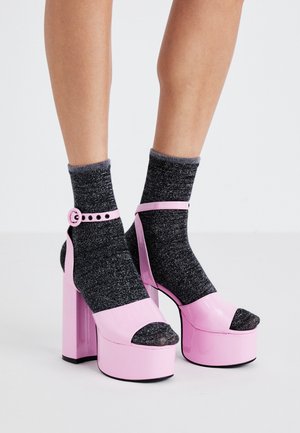 Jambes portant des chaussettes courtes gris foncé pailletées, associées à des sandales à plateforme à talons hauts larges rose clair avec des brides à la cheville.