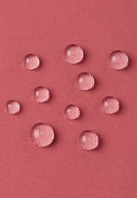 Gocce d'acqua su una superficie tessile rosa strutturata, di varie dimensioni e che riflettono la luce, che mette in risalto il materiale e la qualità tattile.